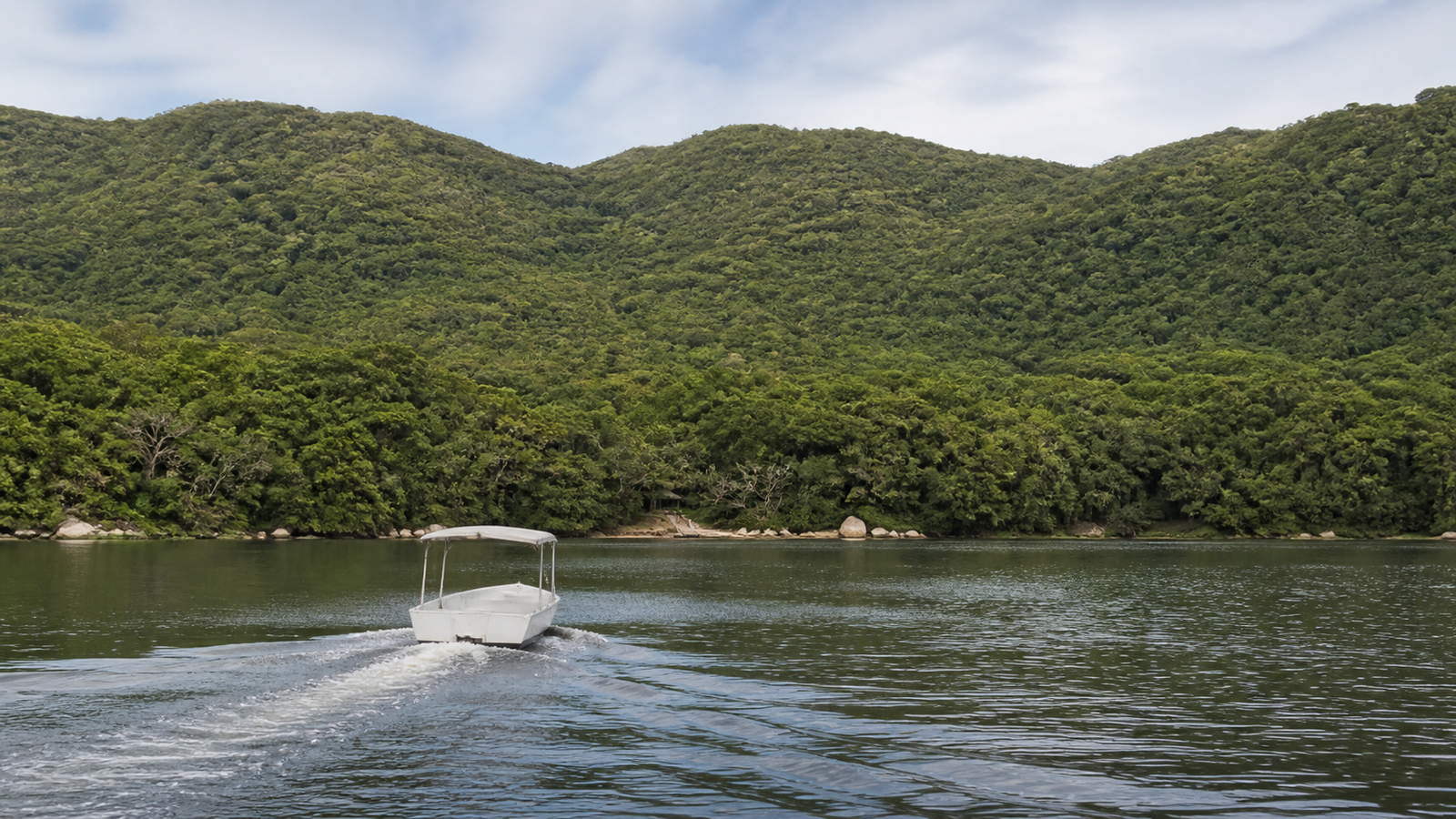 Lagoa da Conceição in half a day: the plan that avoids backtracking 3 Small passenger boat on lagoon water near a forested Costa da Lagoa shoreline.