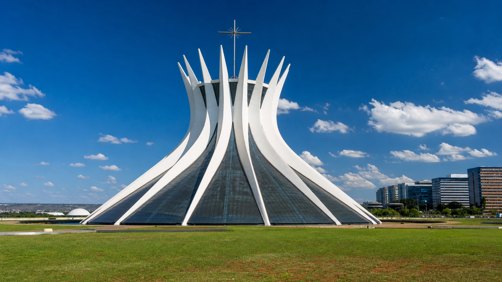 Exterior view of the Cathedral of Brasília with 16 curved white concrete columns reaching into a clear blue sky