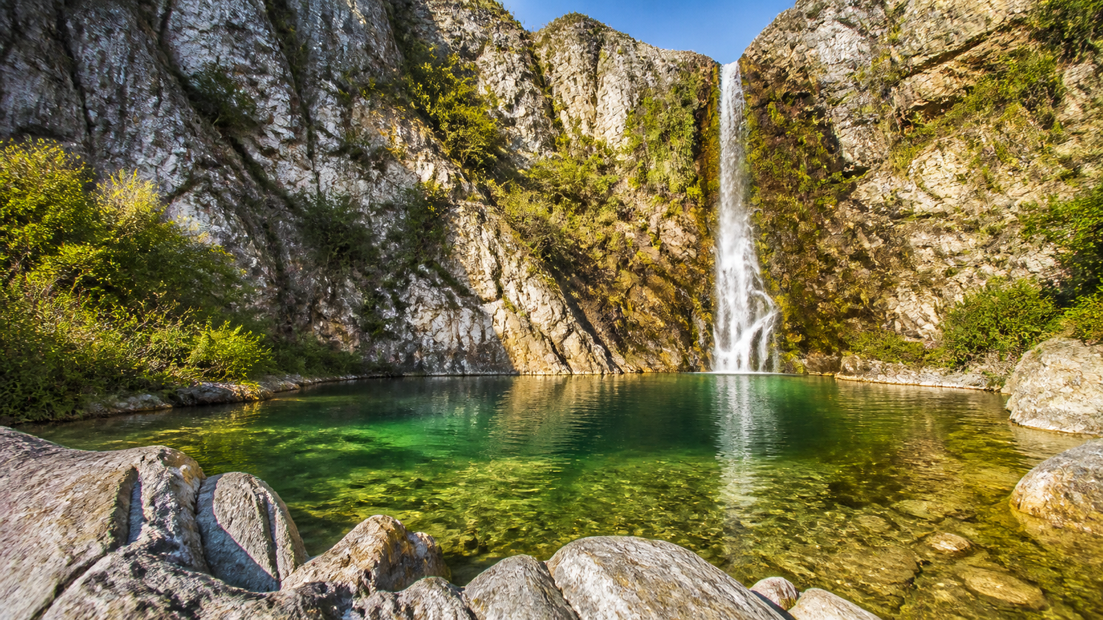 A secluded crystal-clear emerald natural pool surrounded by dramatic rocky canyon walls in Chapada dos Veadeiros, Brazil.