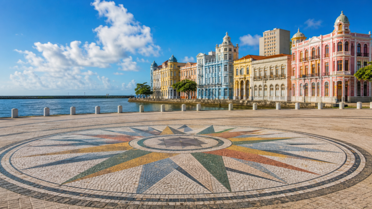 Sunny wide-angle view of Marco Zero in Recife Antigo featuring the colorful Rosa dos Ventos ground mosaic and historic waterfront buildings.