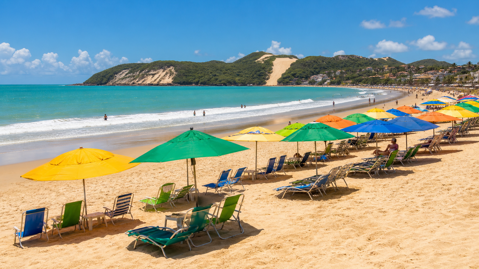 Morro do Careca in Natal: How to Visit Without Wasting Time or Money 3 Colorful beach umbrellas and lounge chairs on the sand of Ponta Negra beach facing Morro do Careca in Natal.