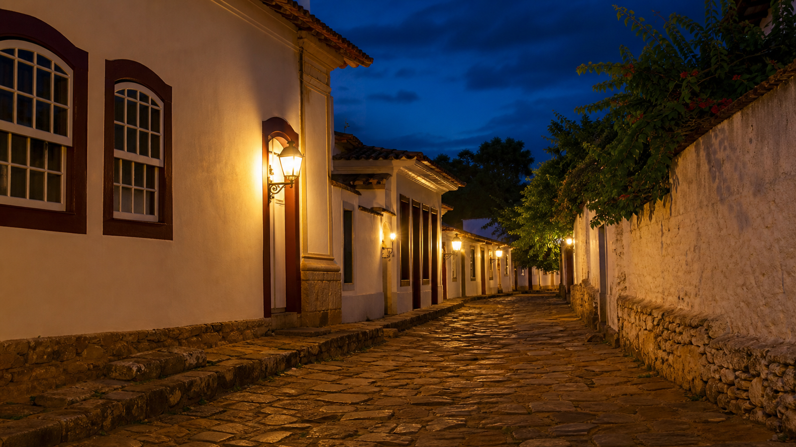 Atmospheric twilight alley in colonial Pirenópolis with glowing street lanterns against a deep blue dusk sky.
