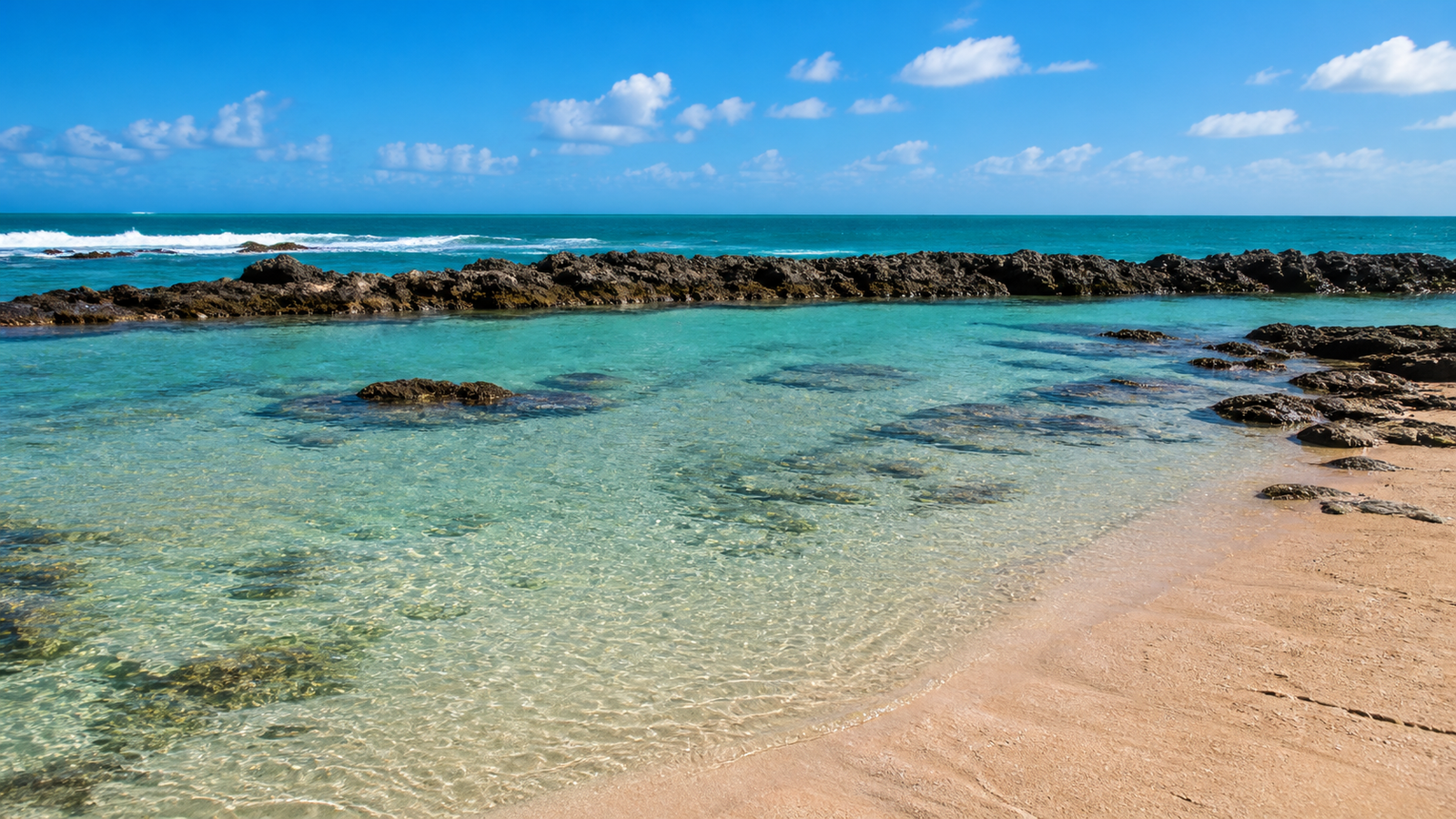 Wave-free natural tidal pools formed by an offshore stone reef barrier on a sunny beach at Praia de Camurupim