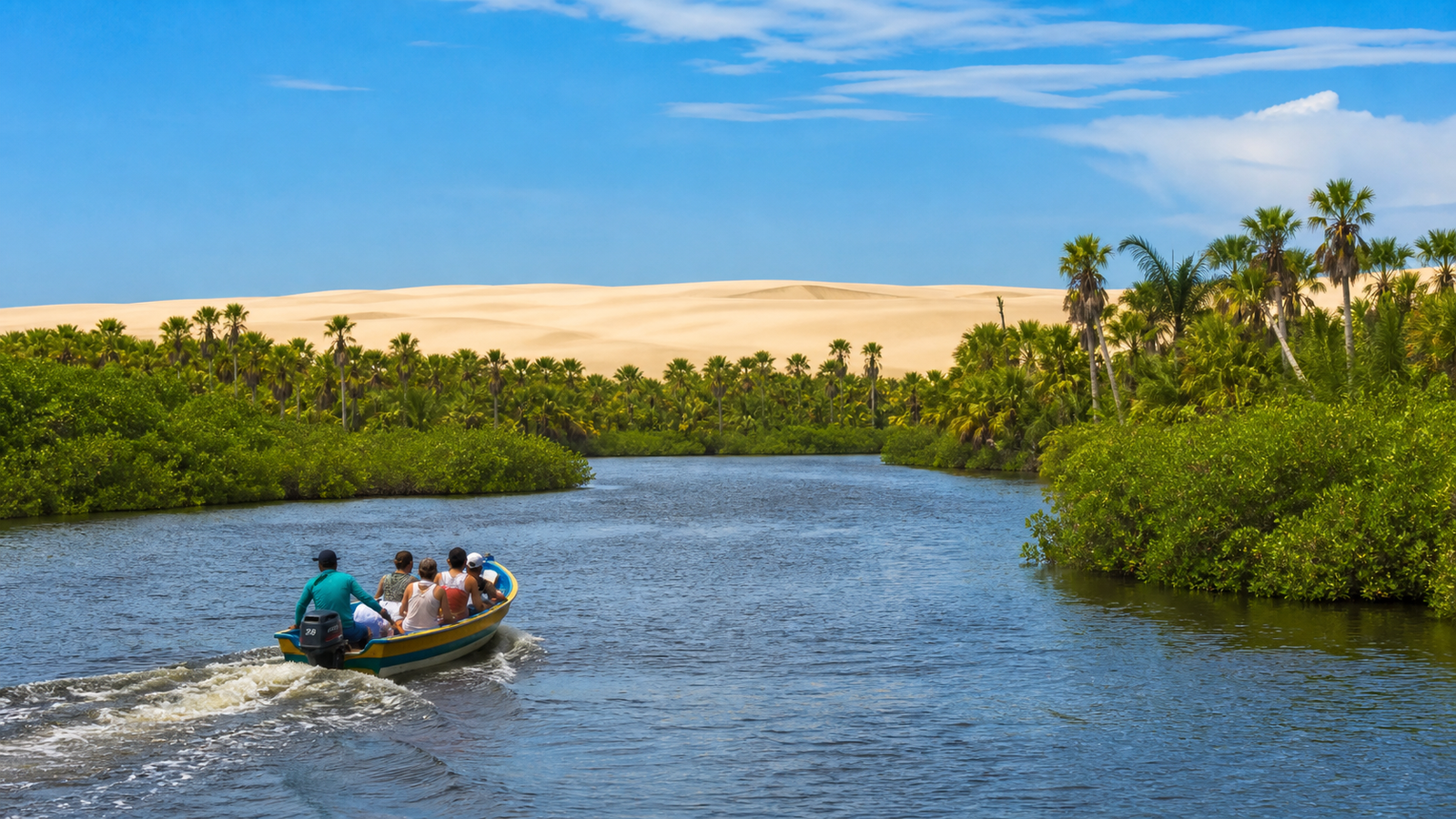 Motorized speedboat navigating down the Preguiças River lined with mangroves and distant sand dunes.