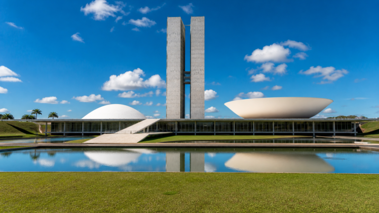 The National Congress of Brazil in Brasília with its iconic twin towers and legislative domes reflected in water under a clear blue sky