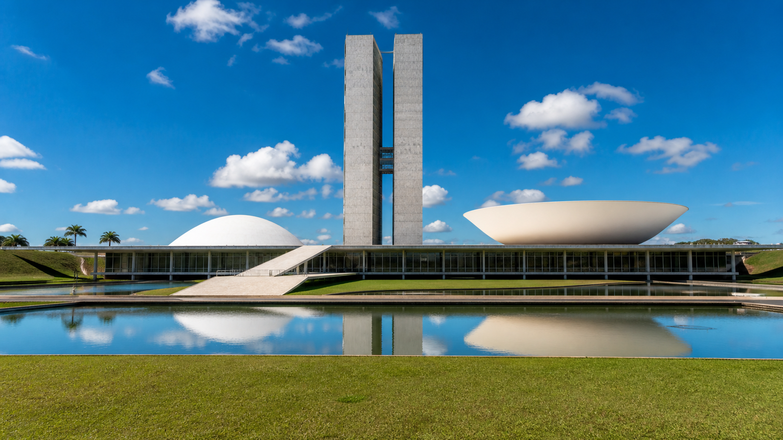 The National Congress of Brazil in Brasília with its iconic twin towers and legislative domes reflected in water under a clear blue sky