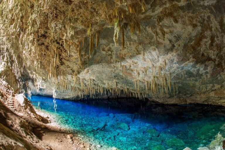 Lago de água azul intensa no fundo da Gruta do Lago Azul, em Bonito (MS), com paredes de calcário e espeleotemas pendendo do teto da caverna
