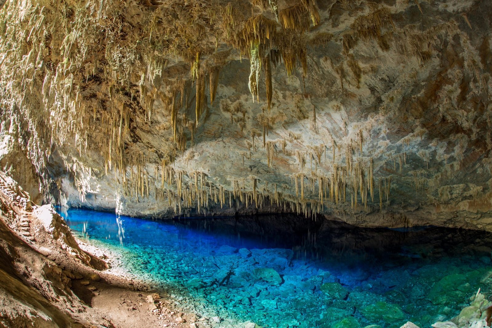 Lago de água azul intensa no fundo da Gruta do Lago Azul, em Bonito (MS), com paredes de calcário e espeleotemas pendendo do teto da caverna