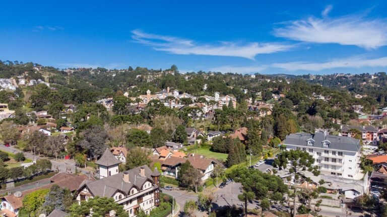 Vista aérea de Vila Capivari, em Campos do Jordão, com casas e hotéis em estilo europeu de telhados escuros, ruas arborizadas e morros cobertos de araucárias sob céu azul