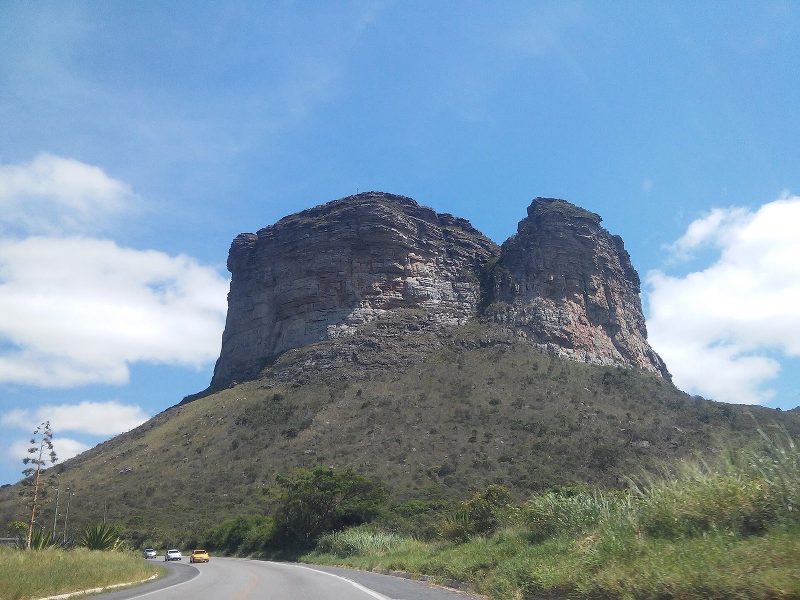 Morro do Pai Inácio, um morro de topo plano e paredões de arenito, visto da estrada BR-242 sob céu azul com nuvens, com vegetação de campo nas encostas