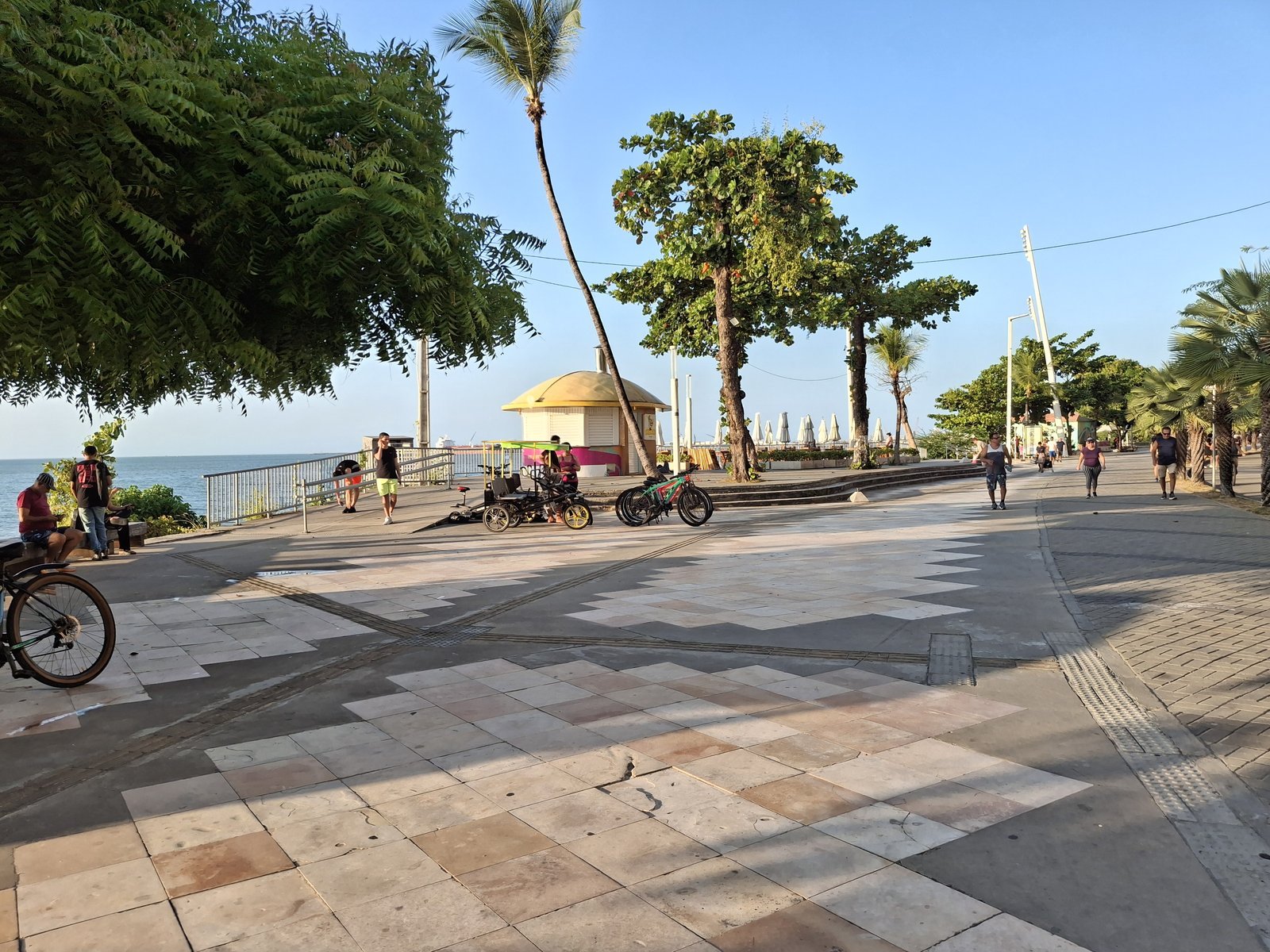 The wide seafront promenade on Avenida Beira-Mar in Fortaleza, Brazil, with palm trees, cyclists and people walking in the afternoon and the sea in the background