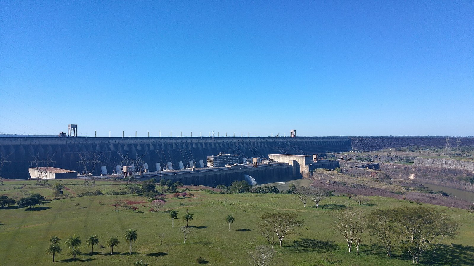 Itaipu Dam seen from a viewpoint, with lawns in front and a clear blue sky