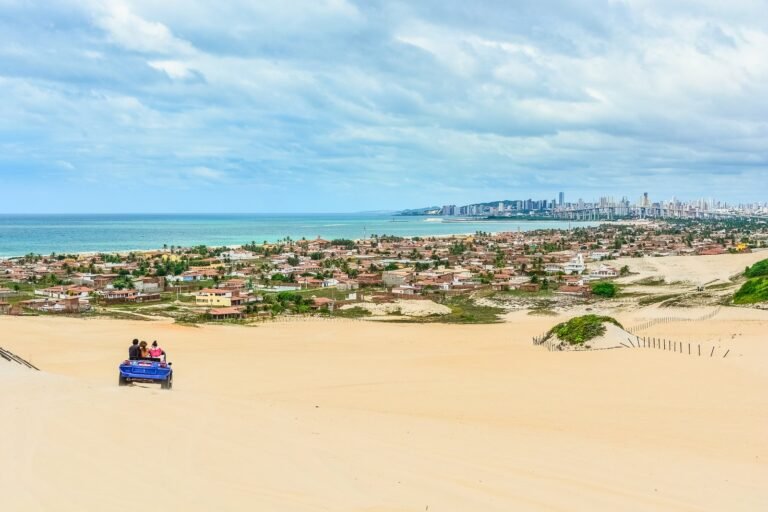 Buggy descendo as dunas de areia clara de Genipabu, no litoral norte do Rio Grande do Norte, com a cidade de Natal ao fundo