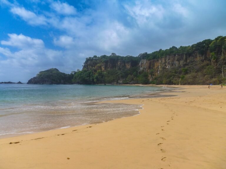 Baía do Sancho em Fernando de Noronha, com faixa de areia dourada, mar verde-azulado e o paredão de falésias coberto de vegetação ao fundo