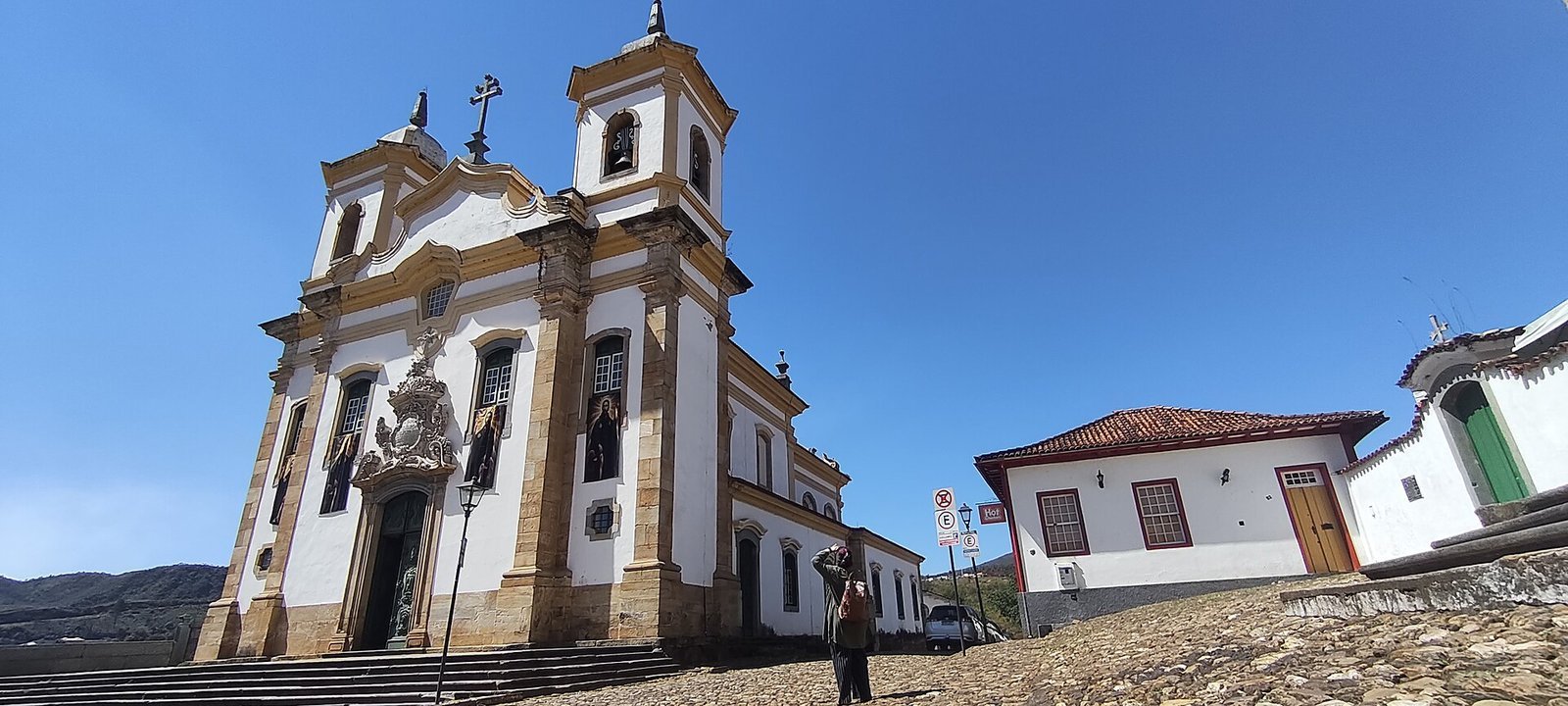O que fazer em Ouro Preto: guia completo 2026 com história, igrejas, minas, preços, roteiro e onde ficar 5 Praça Minas Gerais em Mariana, com a Igreja de São Francisco de Assis de fachada branca e torres, gramado e casarões coloniais em volta sob céu azul