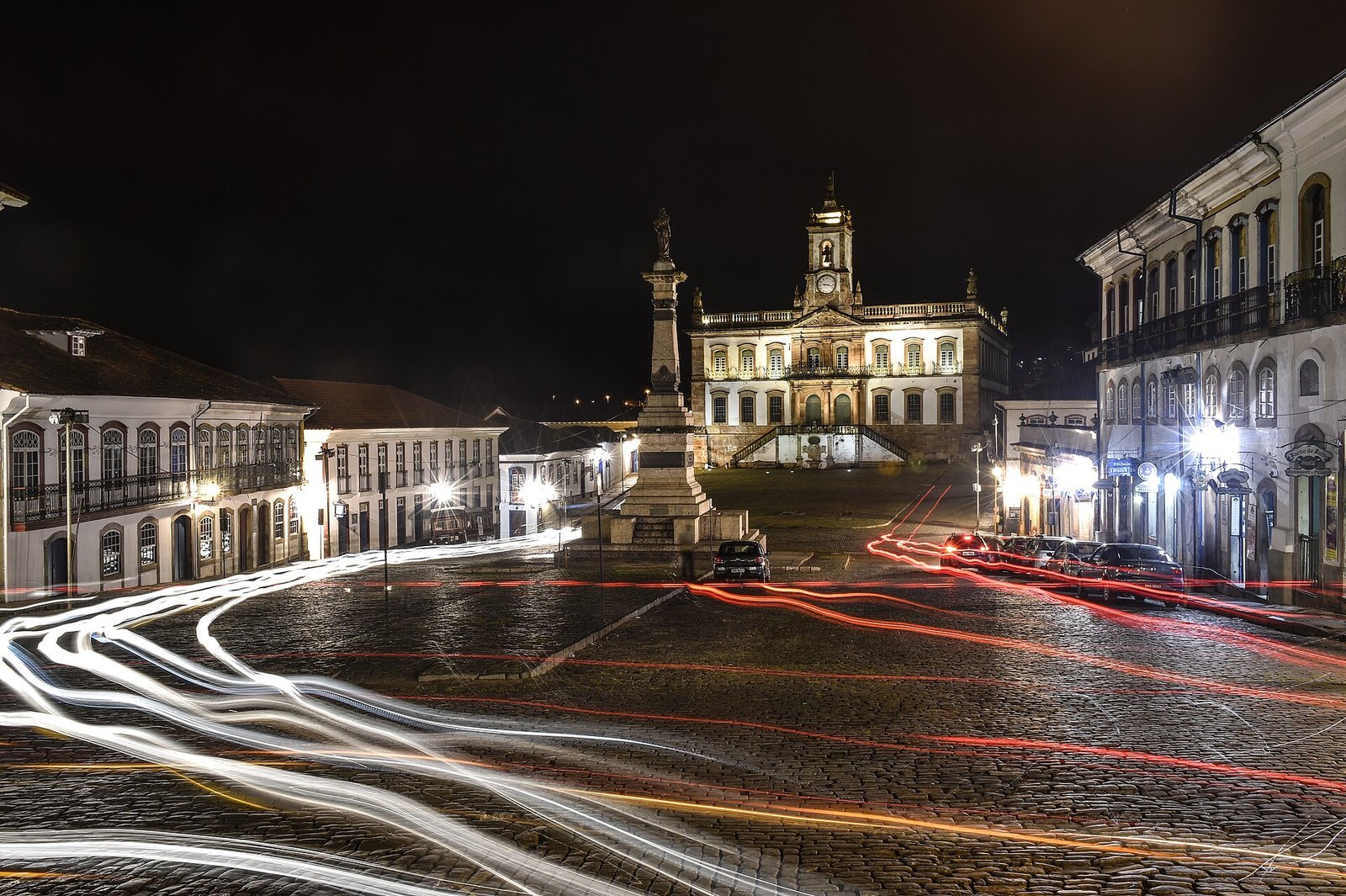 O que fazer em Ouro Preto: guia completo 2026 com história, igrejas, minas, preços, roteiro e onde ficar 3 Praça Tiradentes em Ouro Preto à noite, com o monumento a Tiradentes iluminado, rastros de luz dos carros e os casarões coloniais acesos em volta