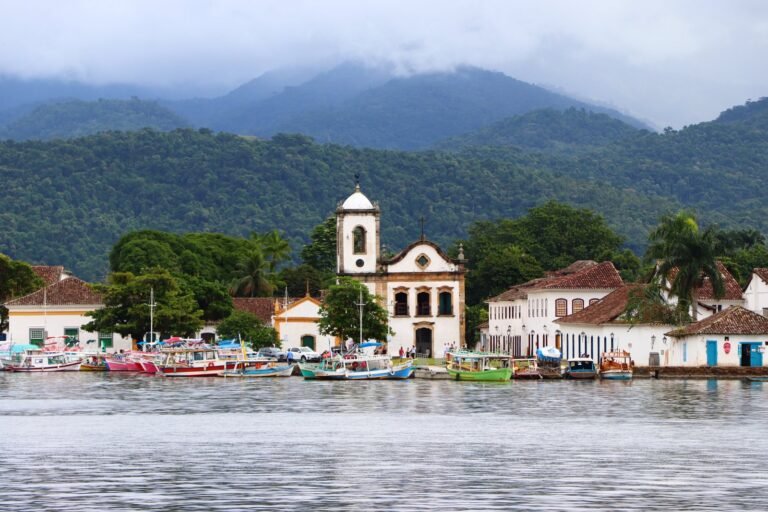 Igreja de Santa Rita vista da água em Paraty, com barcos coloridos e a Serra da Bocaina ao fundo