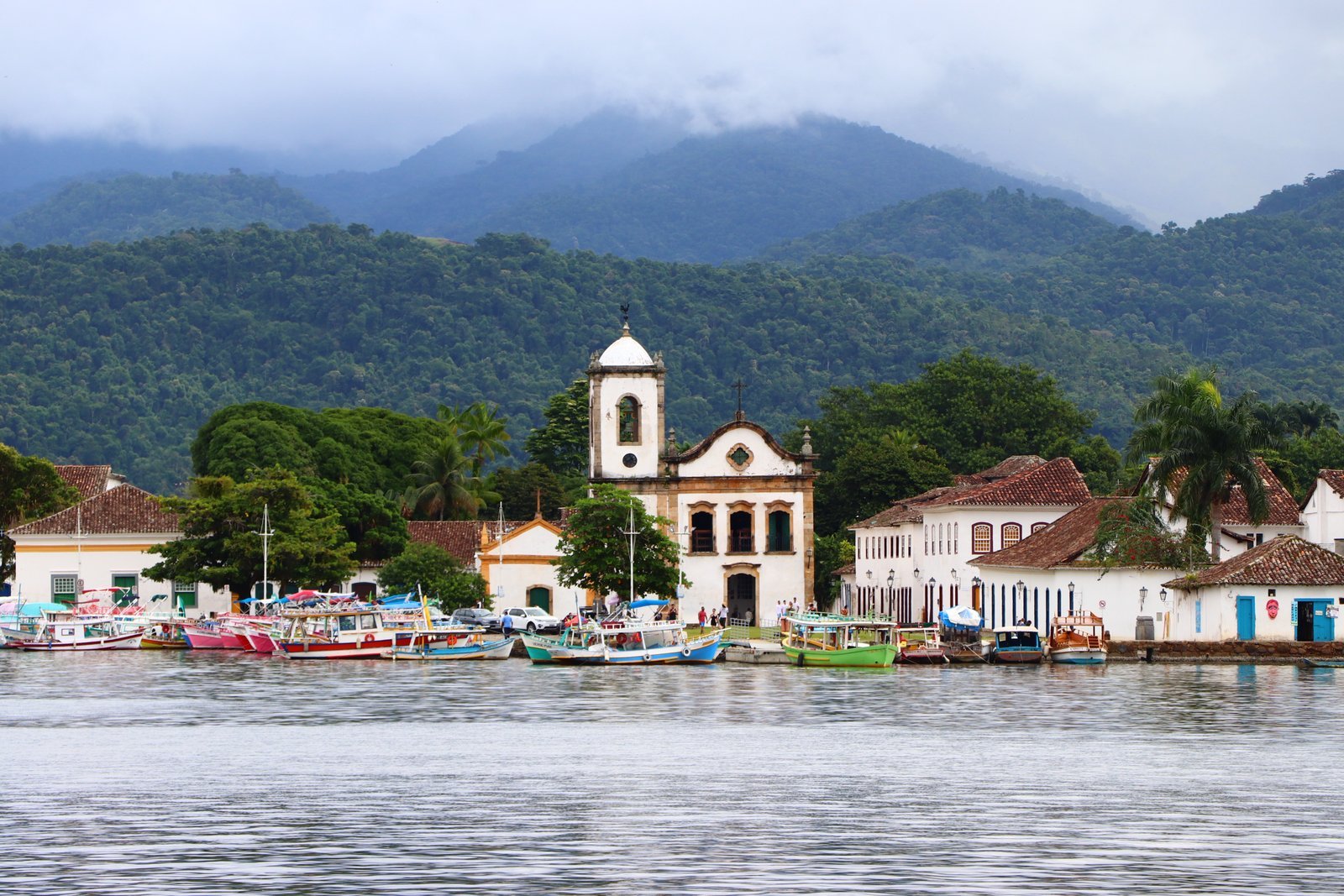 Igreja de Santa Rita vista da água em Paraty, com barcos coloridos e a Serra da Bocaina ao fundo