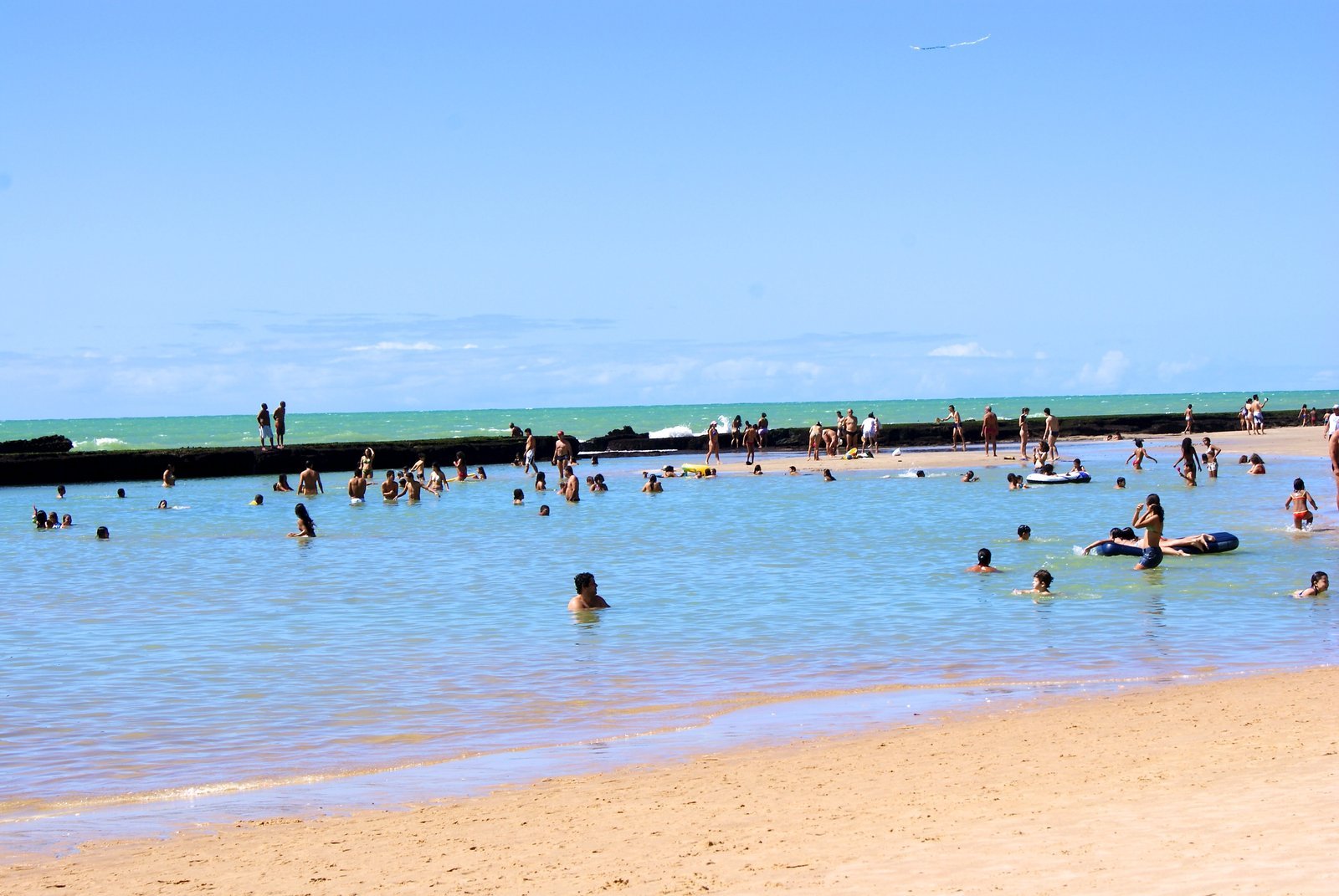 Turquoise natural pool at Boa Viagem beach in Recife, with swimmers in calm water sheltered by the reef in the background and light sand in the foreground