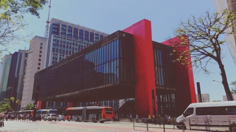 Prédio do MASP na Avenida Paulista, em São Paulo, com a caixa de vidro suspensa por quatro pilares vermelhos e o vão livre aberto para a calçada